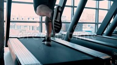 一个穿着运动鞋的男人在现代健身房的跑步机上跑步，上面有全景窗